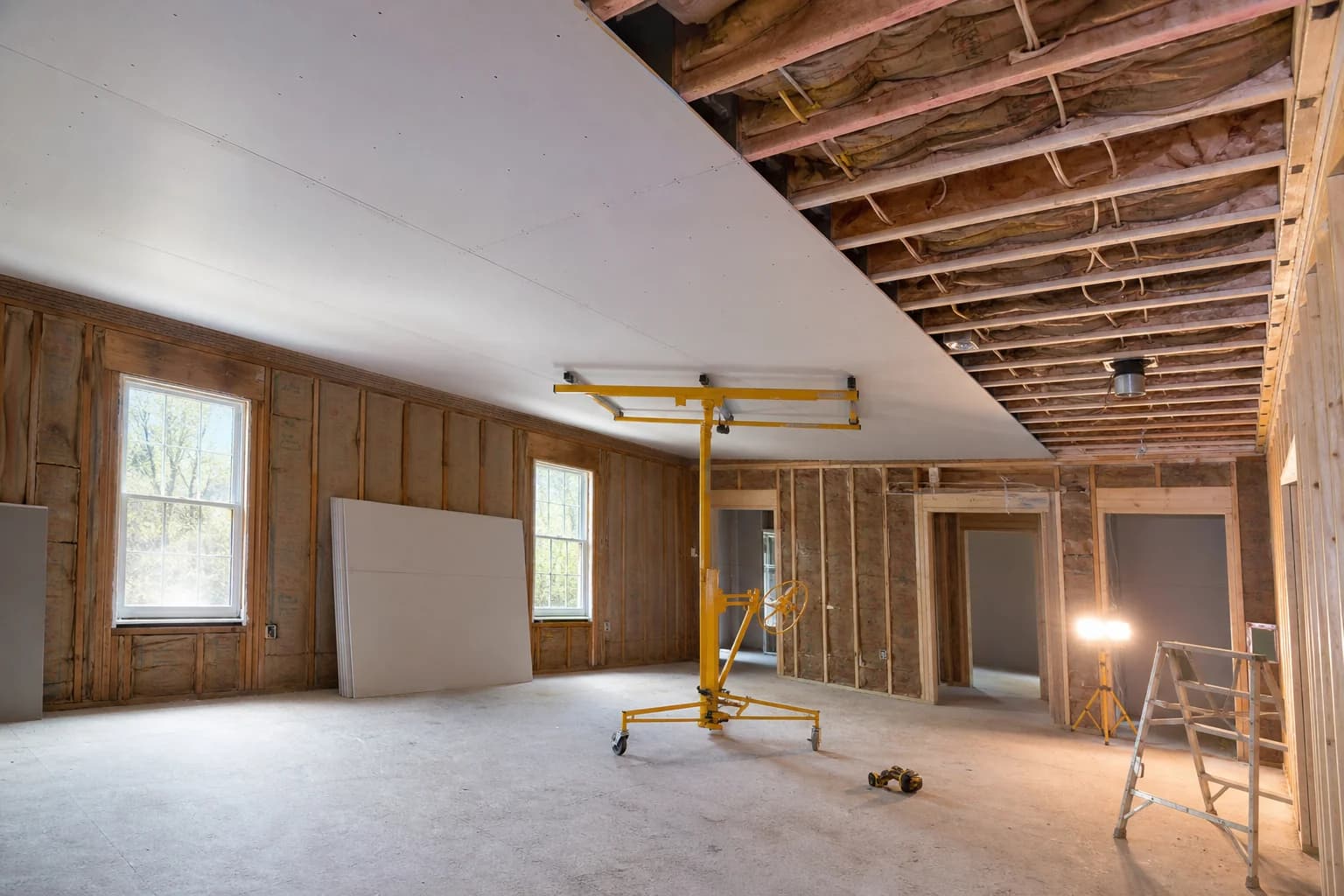 Residential room with drywall ceiling sheets being installed on ceiling joists